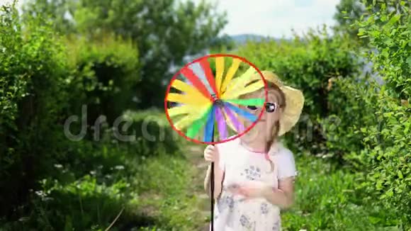 一个小可爱的女孩在温暖的一天在花园里玩一个五颜六色的风车视频的预览图