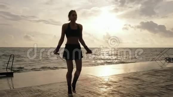 年轻女子在海滩边的阳光下慢慢地用跳绳镜头耀斑一个女孩在跳视频的预览图