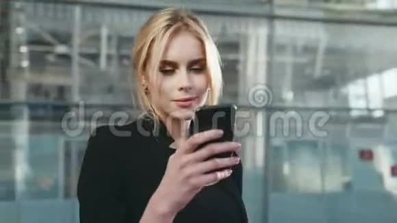 在机场候机楼里一位身穿黑色优雅上衣身穿智能手机的年轻金发美女旋转视频的预览图