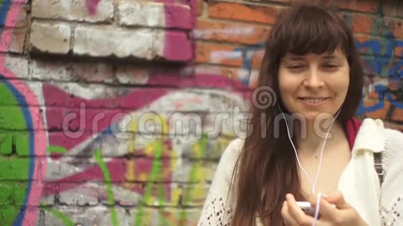 戴着耳机听着墙边涂鸦音乐的年轻女子视频的预览图