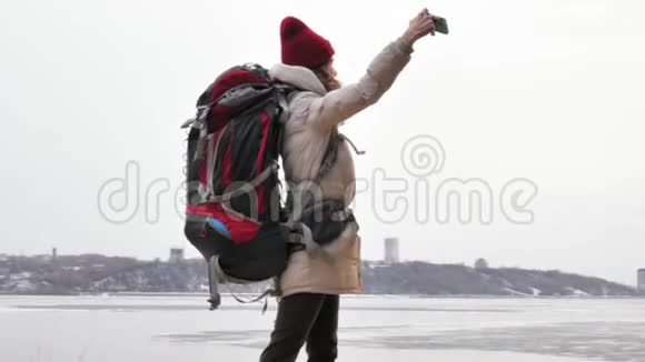 早春一位戴着红帽子的漂亮年轻女子背着一个大旅游背包走过森林带着一个小女孩视频的预览图
