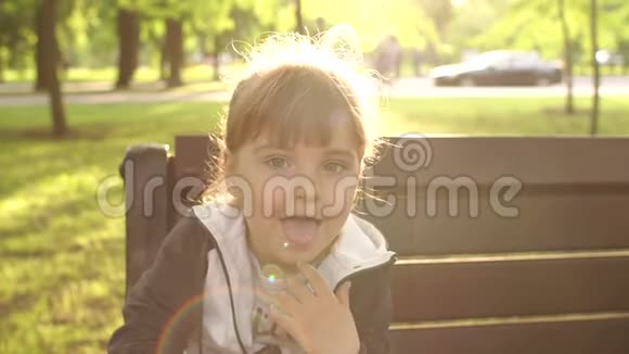 坐在公园长凳上露舌头的小女孩视频的预览图