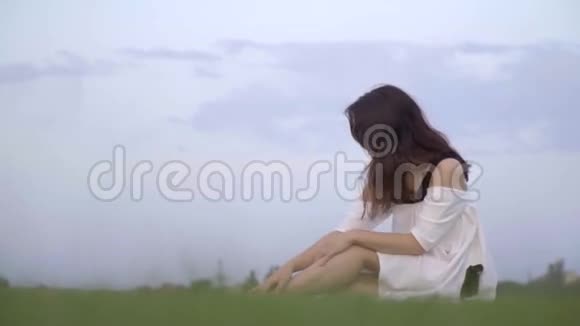日本女孩穿着白色连衣裙微笑着回首坐在草坪上慢动作视频的预览图