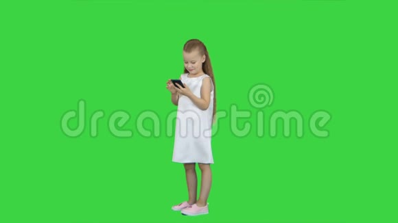 可爱的小女孩微笑用手机在绿色屏幕色度键视频的预览图