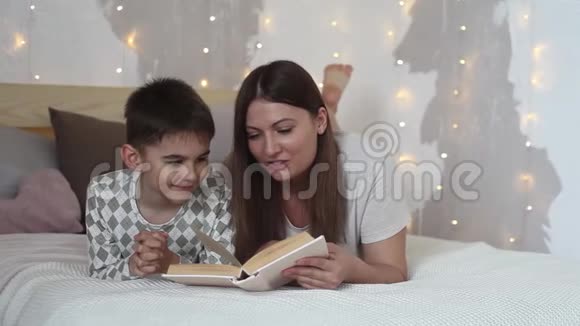美丽的女孩读一本书给躺在床上的小男孩吻他视频的预览图