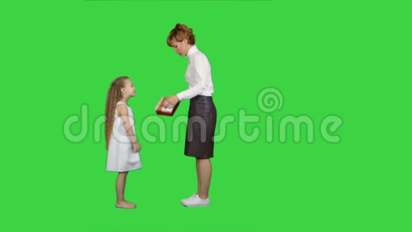 美丽的年轻妈妈在绿色的屏幕上给她迷人的小女孩送礼物彩色钥匙视频的预览图