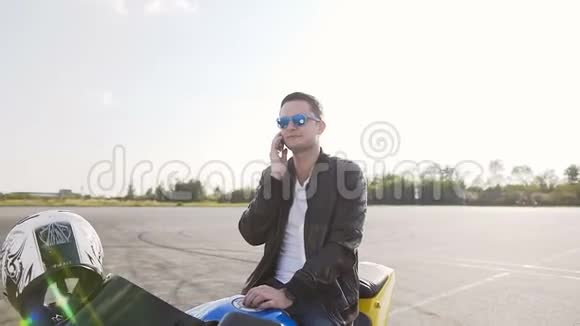 日落时分一个穿着皮夹克的年轻人坐在摩托车上在电话里说着有趣的话视频的预览图