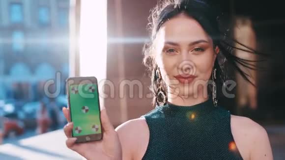 迷人的女人把手机屏幕上的绿色屏幕对着镜头迷人地微笑室外射击视频的预览图