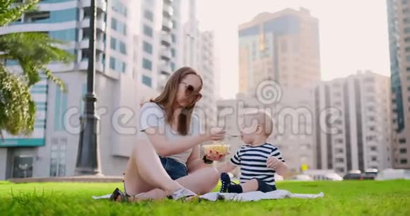 年轻的妈妈带着孩子坐在公园的草地上吃午饭视频的预览图