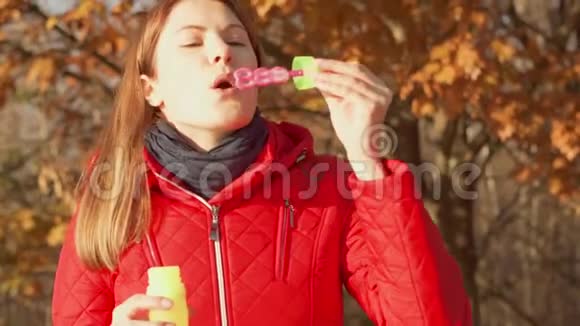 快乐的微笑女人享受大自然站在秋天的公园里穿着红色外套的女性制造肥皂泡视频的预览图