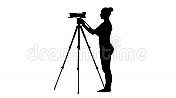 操作人员的剪影在三脚架上操作相机白色背景视频的预览图