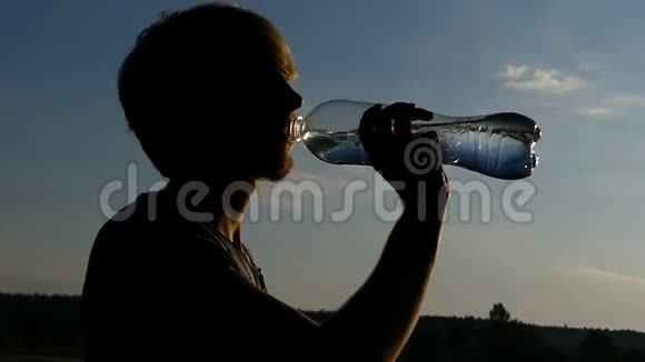 在日落时分金发男人从塑料瓶里喝水视频的预览图
