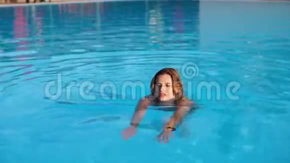 年轻漂亮的金发女郎在游泳池游泳然后展示身体视频的预览图
