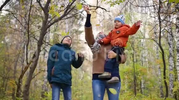 秋天公园里有孩子的女孩扔黄叶微笑着幸福的家庭视频的预览图