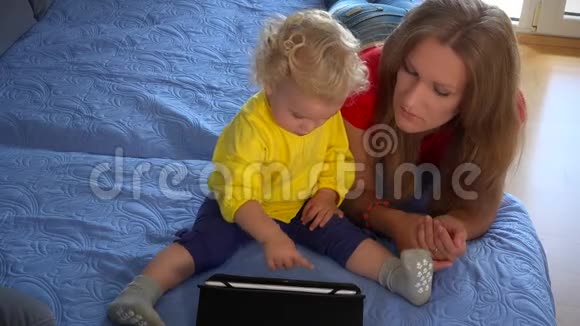 母亲和婴儿在家里的沙发上玩平板电脑视频的预览图