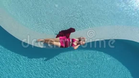 年轻的金发女郎穿着红裙子躺在游泳池里视频的预览图
