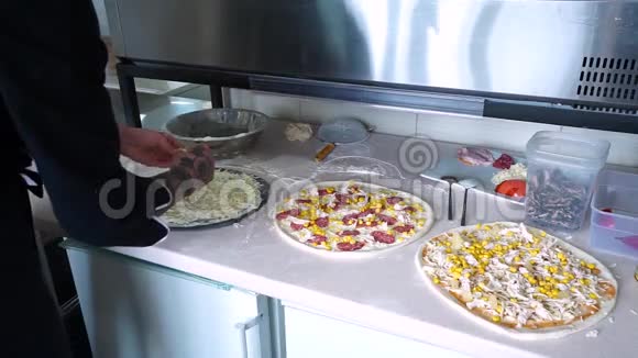 一个年轻的披萨师在餐厅的厨房准备披萨准备黑色披萨厨师把磨碎的东西倒了视频的预览图