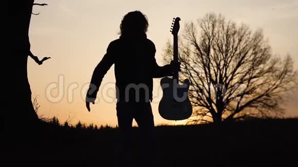 日落时分人们在靠近树的田野里弹电吉他唱抒情歌曲剪影视频的预览图