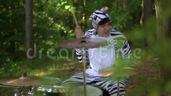 穿着斑马服装的人打鼓微笑享受在树林间疯狂鼓手正在演奏音乐视频的预览图