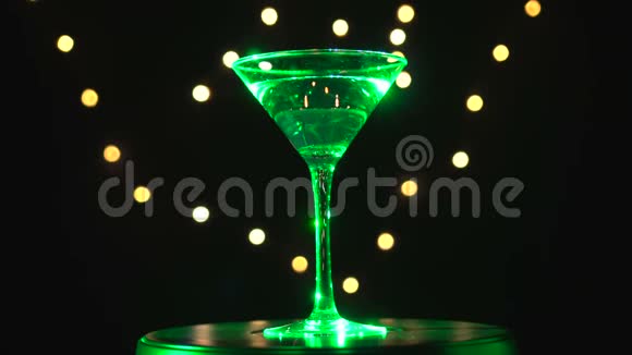 明亮的绿色鸡尾酒在玻璃旋转在黑暗的背景与模糊的光视频的预览图