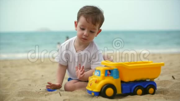 两岁漂亮的婴儿学步男孩骑着玩具货车在夏季海滩特写慢动作视频的预览图