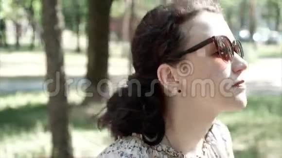 戴墨镜的漂亮黑发女人在夏天的公园里散步视频的预览图