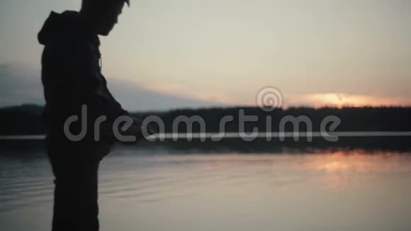 剪影男向日落湖扔石头视频的预览图