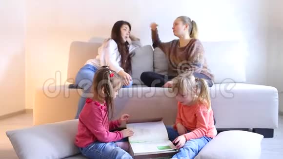 两个女孩坐在地板上翻书年轻妈妈坐在沙发旁边讨论问题视频的预览图