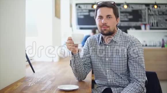 一个年轻人手里拿着一杯茶或咖啡在咖啡馆里的肖像视频的预览图