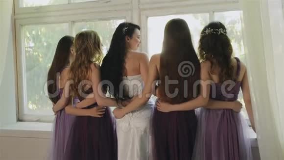 新娘在工作室里和伴娘拥抱穿紫色连衣裙的漂亮女孩嘲笑窗户妇女视频的预览图