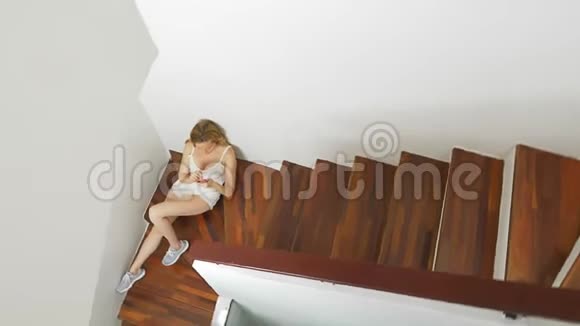 穿短裤的女孩坐在家里的楼梯上使用智能手机视频的预览图