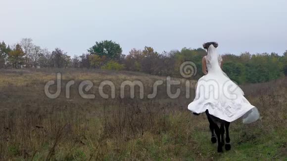 穿着白色婚纱骑马穿过田野的年轻女子视频的预览图