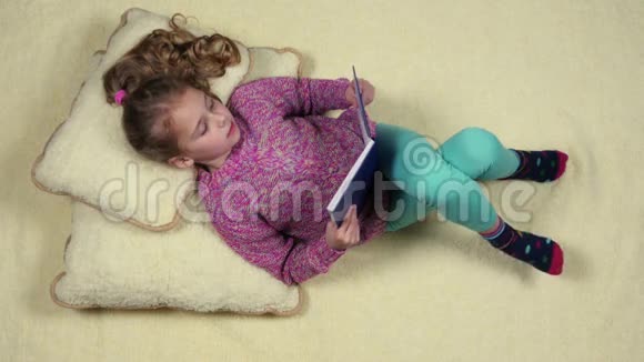 有趣的小女孩躺在沙发上看书顶部视图视频的预览图
