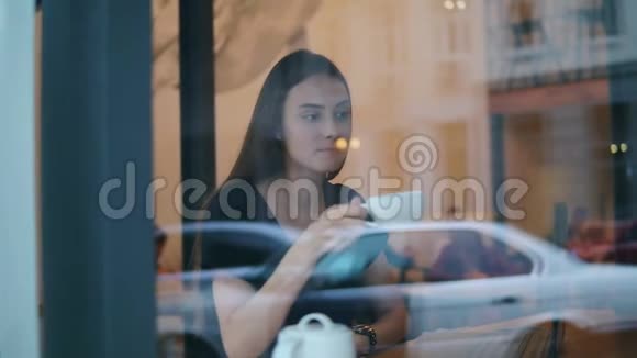 从街上看到一个年轻的女人在咖啡店坐着的咖啡馆里喝茶或咖啡视频的预览图