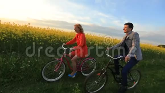 快乐的爱人在日落时骑自行车沿着美丽的盛开的田野玩得很开心视频的预览图