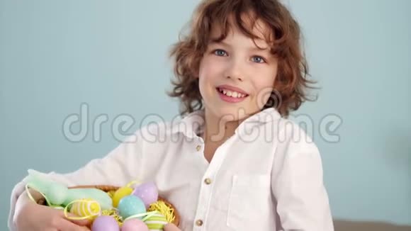 卷曲的红发孩子穿着白色衬衫有一只复活节兔子的身影篮子里有一套复活节彩蛋一个男孩视频的预览图