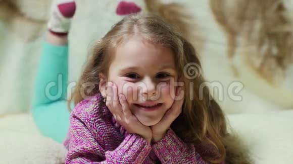 美丽的小女孩对着镜头微笑躺在沙发上的快乐孩子的肖像视频的预览图