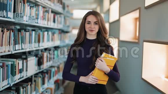 留着长发的女孩微笑着直视着图书馆书架前的镜头视频的预览图