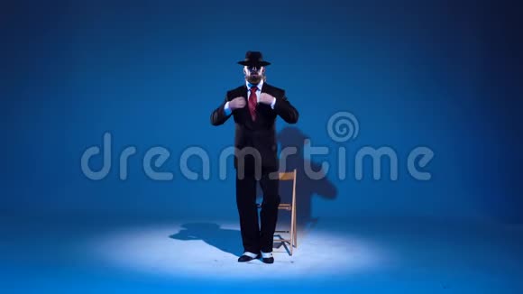戴着黑帽子的优雅男人正在跳情色舞在蓝色背景上聚光灯视频的预览图