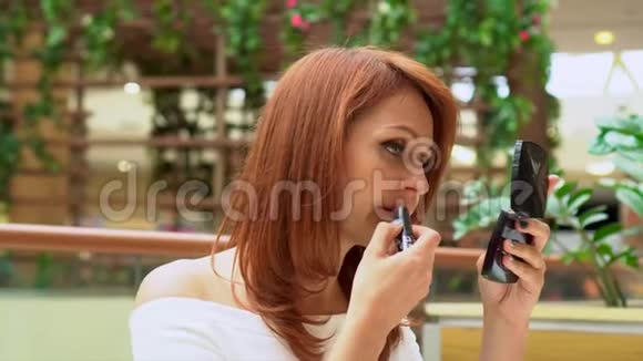 那个女人在购物中心化妆这位年轻女子在商场里照了照口袋里的镜子并用嘴唇视频的预览图