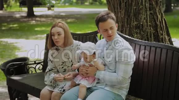 一个小快乐的孩子和他的父母在公园的长凳上吃玉米棒视频的预览图