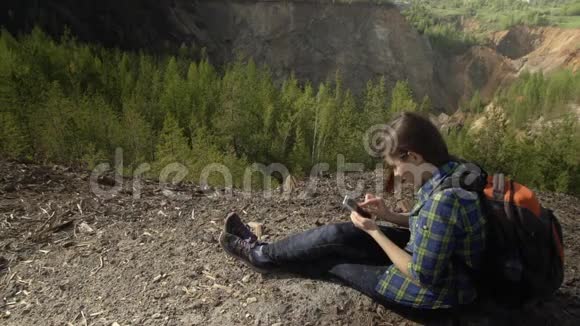 一个年轻的女人坐在山上享受智能手机视频的预览图