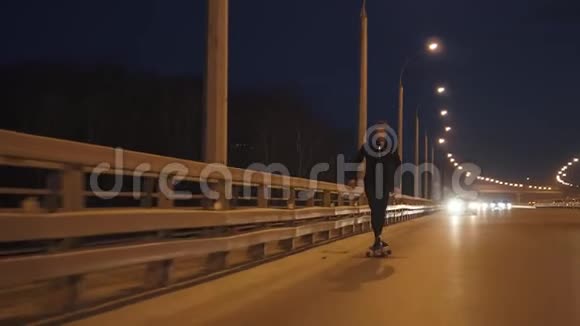 晚上他骑着长板穿过城市年轻人晚上在路上滑冰慢动作视频的预览图