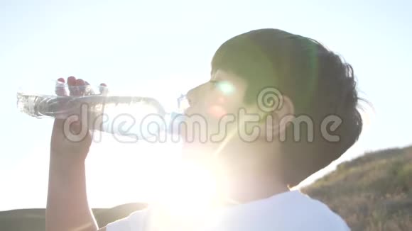 日落时分男孩从塑料瓶里喝水太阳光线穿过视频的预览图