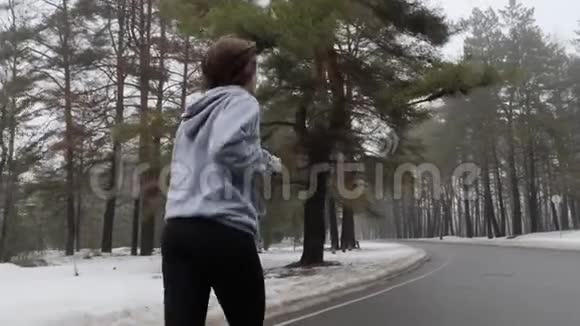 年轻迷人的白种人女孩在冬天带着耳机在雪地公园跑步后面跟着射击慢动作视频的预览图