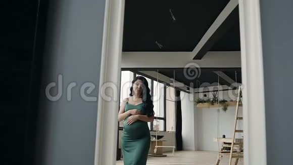 美丽的怀孕少女穿着绿色晚礼服照镜子视频的预览图