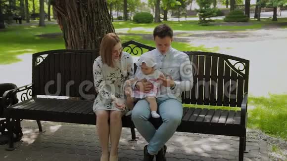 一个小快乐的孩子和他的父母在公园的长凳上吃玉米棒视频的预览图
