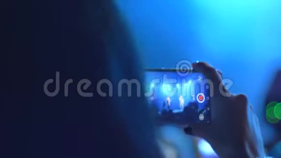 观众在非聚焦背景下的夜间音乐会特写镜头上用手机录制视频视频的预览图