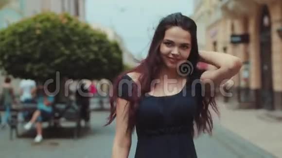 可爱的年轻黑发女人穿着黑色休闲服走在市中心的街道上转过身来微笑着走向中央视频的预览图