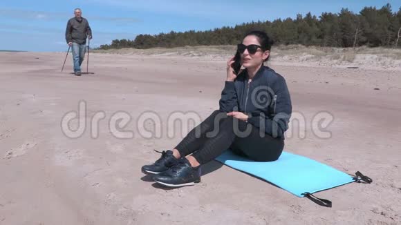女人坐在海边的健身垫上在智能手机上聊天视频的预览图